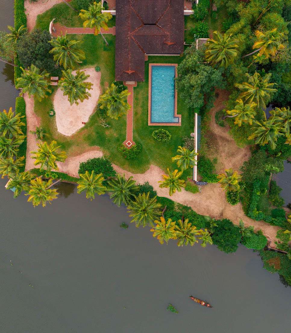Aerial view of Vembanad Lake backwaters at dawn — still green water, coconut palms and the mist of a Kerala morning