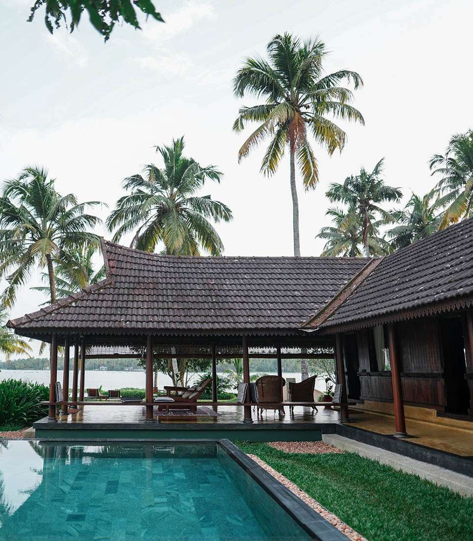 The entrance hall of Vismaya — teak beams, terracotta floor and the green light of the lake filtering through old wooden screens